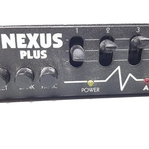 May include: Black audio mixer with the text "NEXUS PLUS" and five knobs. The mixer has a power indicator light and a series of five switches labeled 1 through 5. The mixer also has two red indicator lights labeled "A" and "B".