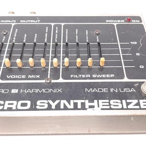 Könnte beinhalten: Ein schwarzer und silberner Electro Harmonix Micro Synthesizer mit Knöpfen und Schiebereglern. Der Text "ELECTRO HARMONIX" und "MICRO SYNTHESIZER" ist auf der Vorderseite des Geräts aufgedruckt. Der Netzschalter ist eingeschaltet und die rote LED leuchtet.