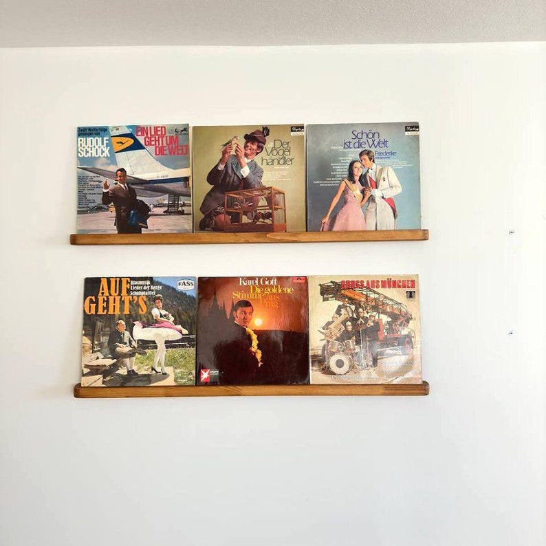 May include: Two wooden shelves with a collection of vintage vinyl records. The records have various titles and artists, including "Rudolf Schock", "Ein Lied", "Der Vogelhandler", "Schon ist die Welt", "Auf Geht's", "Karl Gott", and "Grosses aus Wien".