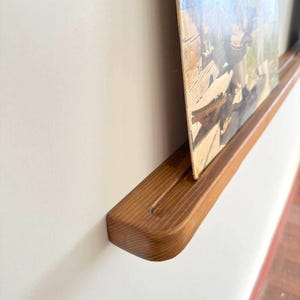 May include: A wooden wall shelf with a rounded edge, designed to hold a vinyl record. The shelf is stained a rich brown color and has a groove to hold the record in place.