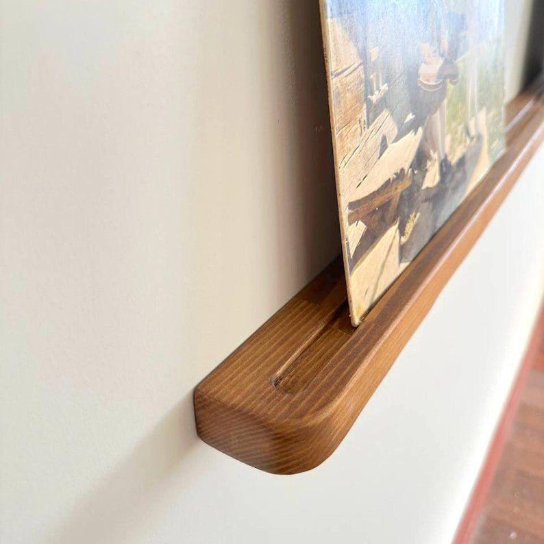 May include: A wooden wall shelf with a rounded edge, designed to hold a vinyl record. The shelf is stained a rich brown color and has a groove to hold the record in place.