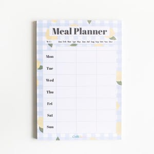 Op de afbeelding: Een witte maaltijdplanner met een blauw-wit geruit patroon en citroenillustraties. De planner heeft een sectie voor elke dag van de week en een rij voor elke maand van het jaar. De tekst "Meal Planner" staat bovenaan de pagina.