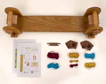 May include: A wooden weaving loom with a natural finish, accompanied by instruction sheets, small wooden cards, and colorful yarn in red, yellow, and blue. The loom is approximately 24 inches wide.
