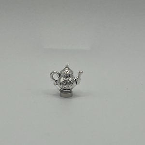 May include: A silver teapot charm with a detailed design. The charm is small and would be perfect for a charm bracelet or necklace.