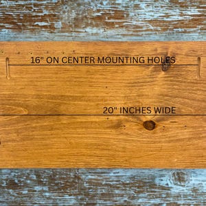 Pu&ograve; includere: Una tavola di legno macchiato con il testo "16" ON CENTER MOUNTING HOLES", "20" INCHES WIDE" e "11" INCHES HIGH". La tavola &egrave; rettangolare con una finitura marrone chiaro e venature del legno visibili. Il testo &egrave; nero.