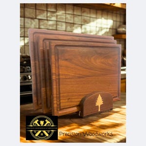 May include: A stack of four square wooden cutting boards with a carved groove around the edges. The boards are displayed in a wooden holder with a tree design. The words "Precision Woodworks" are visible.