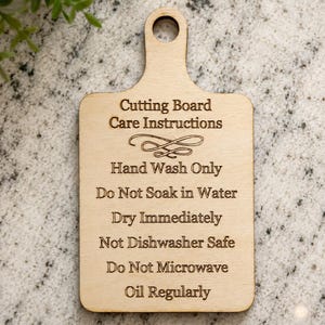 K&ouml;nnte beinhalten: Ein helles Holzschneidebrett mit einem Griffloch, das den lasergravierten Text tr&auml;gt: Cutting Board Care Instructions, Hand Wash Only, Do Not Soak in Water, Dry Immediately, Not Dishwasher Safe, Do Not Microwave und Oil Regularly.