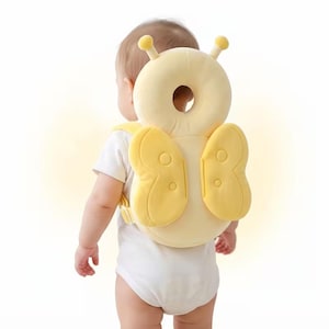 May include: A yellow baby head protector cushion shaped like a butterfly with two antennae on top. The soft, padded accessory features a circular cutout in the center and two wing-shaped side panels, secured with adjustable straps around the torso.
