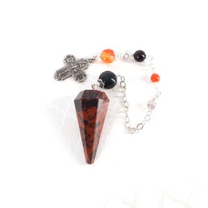 May include: A pendulum featuring a faceted mahogany obsidian point attached to a silver-toned metal chain. The chain includes a silver-toned cross charm and several small, round beads in shades of orange, black, and clear, arranged in a sequence.