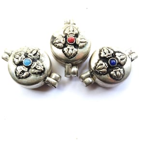 May include: Three silver-toned pendants with ornate floral designs and colored stone accents. Each pendant features a different colored stone: blue, red, and blue. The pendants have a round shape with a loop for hanging.