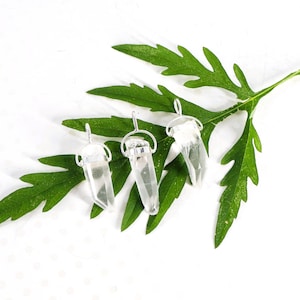 May include: Three clear, pointed quartz crystal pendants, each secured with a silver-toned metal cap and a small circular bail for hanging. The crystals are transparent with natural internal inclusions and are arranged in a row.