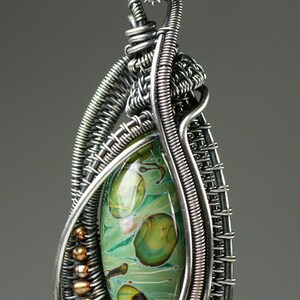 May include: A silver wire wrapped pendant with a green and brown glass stone. The pendant is attached to a silver chain.