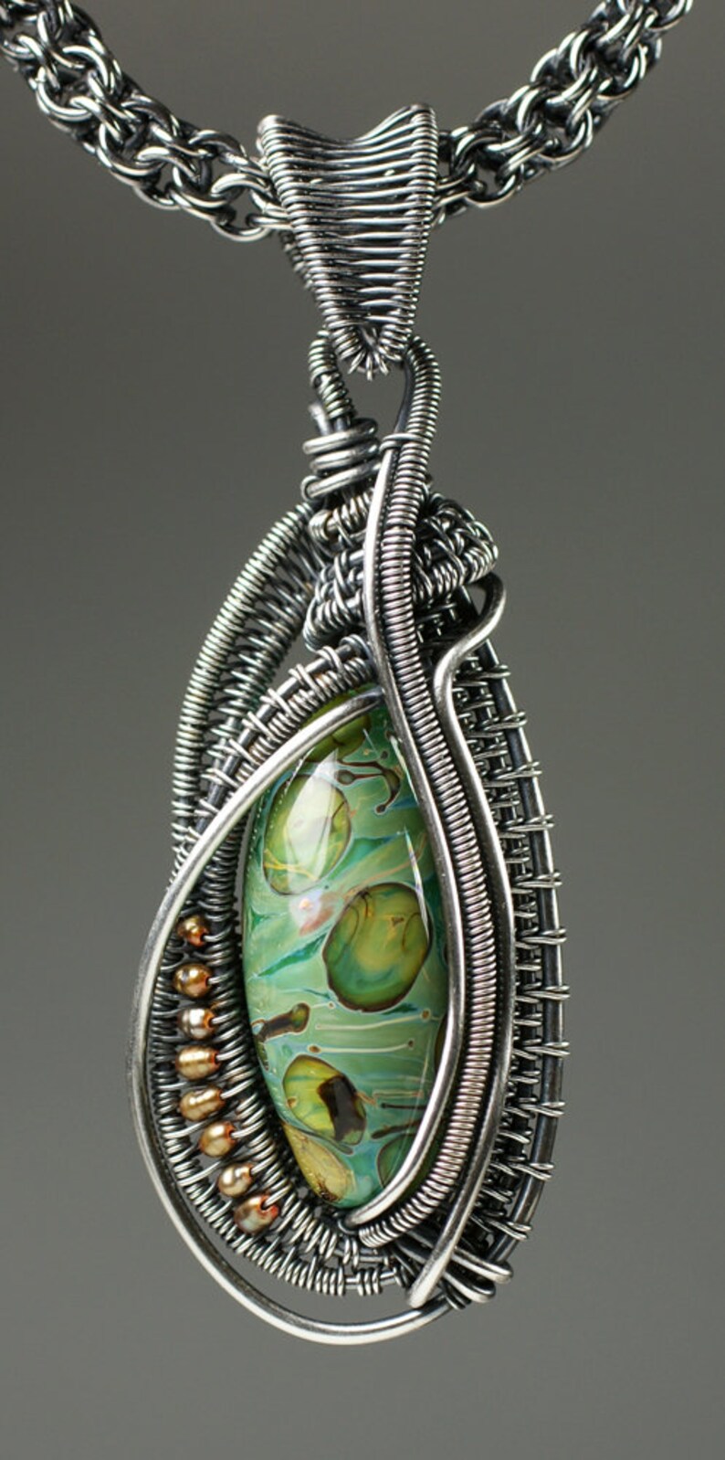 May include: A silver wire wrapped pendant with a green and brown glass stone. The pendant is attached to a silver chain.