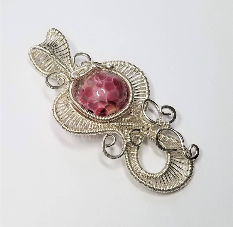 May include: A silver wire wrapped pendant with a pink and white speckled stone in the center.
