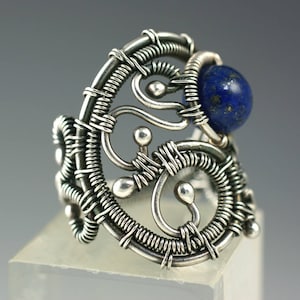 May include: A silver ring with a blue lapis lazuli stone set in a wire-wrapped design. The ring is made of intricate wirework and has a delicate, organic feel.