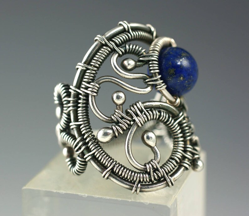 May include: A silver ring with a blue lapis lazuli stone set in a wire-wrapped design. The ring is made of intricate wirework and has a delicate, organic feel.