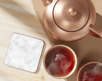 May include: A white marble coaster with a copper teapot and two cups of tea. The tea is steaming and the cups are on a wooden surface.