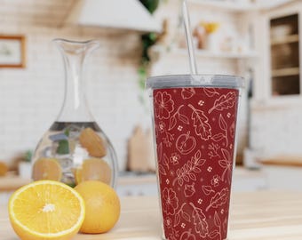 Op de afbeelding: Een rode en witte tumbler met een bloemen- en bladpatroon. De tumbler heeft een doorzichtig deksel en een rietje.