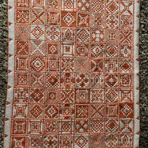 May include: A white crocheted blanket with a repeating pattern of orange and white squares. The blanket is made with a variety of different stitches and textures.