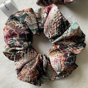 Pode incluir: Um scrunchie marrom, branco e turquesa com um design de pele de cobra. O scrunchie é feito de tecido e tem um visual franzido.