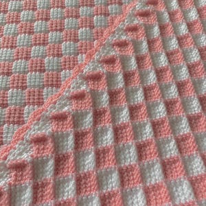 May include: A pink and white checked crochet blanket with a scalloped edge.
