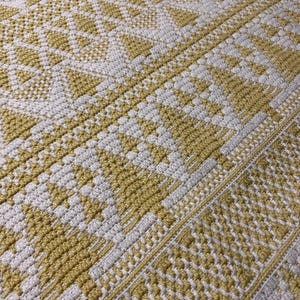 May include: A crocheted throw blanket with a geometric pattern in white and yellow.