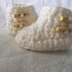 May include: A pair of white crocheted baby booties with yellow button closures.