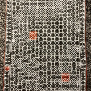 Könnte beinhalten: Eine weiße und schwarze Häkeldecke mit geometrischem Muster. Die Decke hat einen roten und orangen Rand.