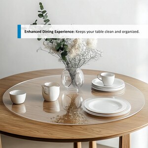 Puede incluir: Un protector de mesa redondo transparente colocado sobre una mesa de madera. El protector est&aacute; dise&ntilde;ado para mantener la mesa limpia y organizada. Un jarr&oacute;n con flores blancas, una taza y un platillo, y una jarra de crema est&aacute;n sobre el protector de mesa.
