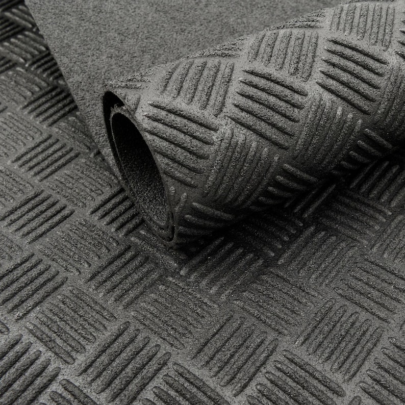 May include: A rolled-up, dark grey rubber mat featuring a diamond plate design. The mat has a textured surface with raised, diagonal lines, providing a non-slip texture. The rolled section shows the mat's thickness.