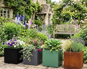 May include: Four square planters in black, gray, green, and rust-colored metal arranged in a row on a stone patio. Each planter contains different plants, including purple and white petunias, red fuchsia, green hostas, and lavender with ornamental grass.