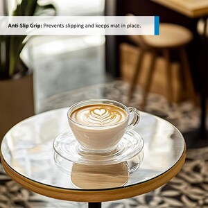 Puede incluir: Una taza de vidrio con un dise&ntilde;o de arte latte se encuentra sobre un platillo de vidrio transparente en una mesa de madera con una tapa de vidrio. El texto "Anti-Slip Grip: Prevents slipping and keeps mat in place." es visible en el fondo.