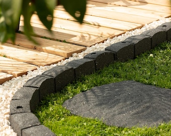 May include: A curved black plastic edging for a garden path, with white gravel and a wooden walkway in the background.