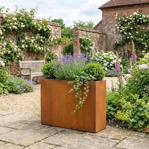 May include: A large, rectangular, weathered metal planter filled with lavender, ivy, and boxwood. The planter sits on a stone patio in a garden, with a brick wall and bench in the background. The planter's dimensions are approximately 100cm x 50cm x 50cm.