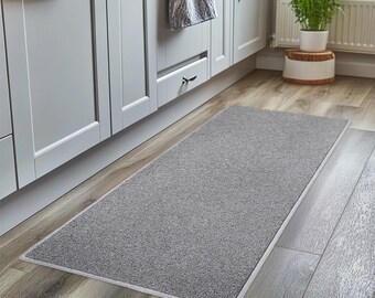 May include: A gray runner rug with a white border, placed in front of a set of kitchen cabinets.