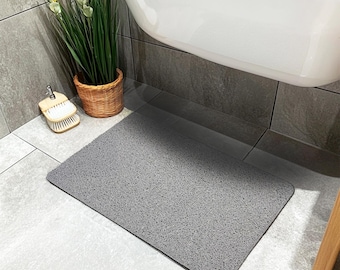 May include: A gray bath mat with a textured surface. The mat is placed on a tiled floor in a bathroom.