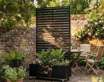 May include: A tall, rectangular black metal planter box featuring a vertical slatted privacy screen. The planter is mounted on small swivel castors and is filled with green ferns and small pink flowers, creating a mobile garden partition.