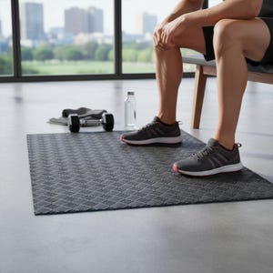 May include: A grey exercise mat with a textured pattern, a dumbbell, a water bottle, and grey athletic shoes with red accents. The scene is set in a room with a large window overlooking a cityscape.