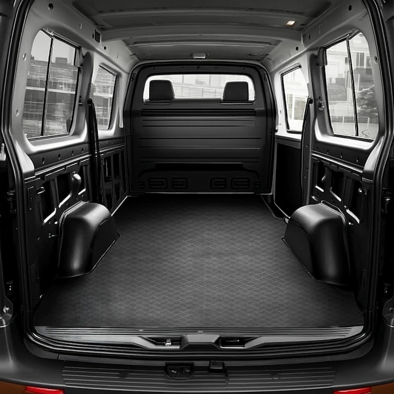 May include: Interior view of a black cargo van, featuring a diamond-patterned floor mat. The van has two rear seats and side windows. The space is empty and well-maintained, ready for cargo.