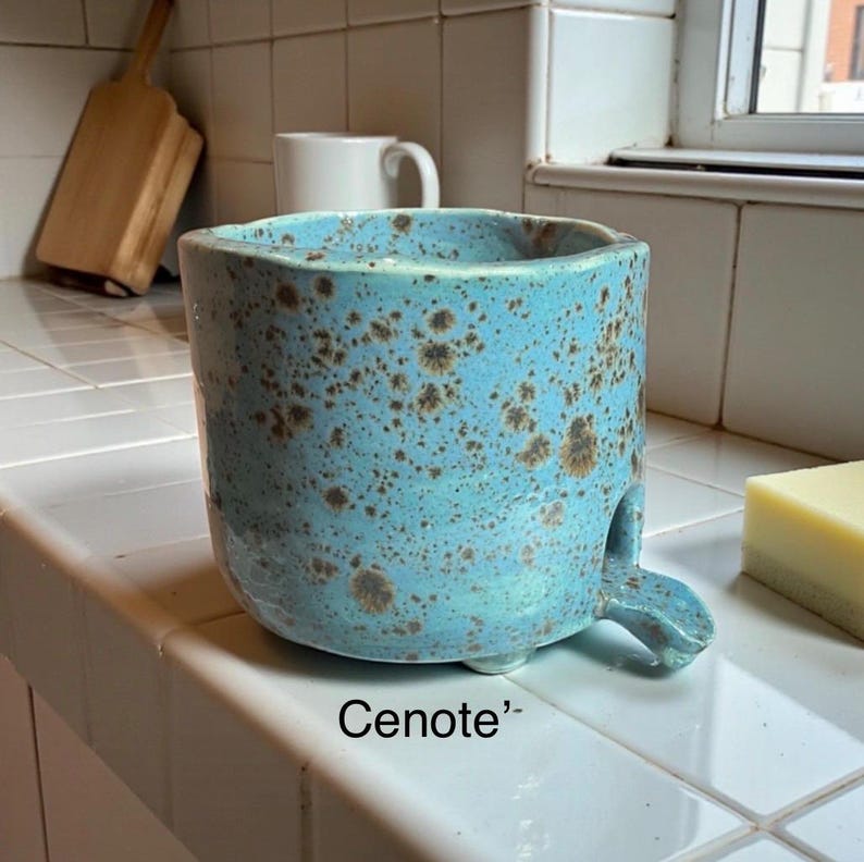 May include: A cylindrical ceramic vessel with a bright turquoise glaze and dark brown speckled texture. The piece features a small, protruding spout at the base and is labeled with the text Cenote. The design includes a wide, open top.