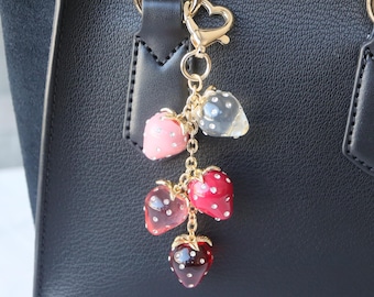 May include: A gold chain keychain with a charm of multiple red, pink, and clear glass strawberries. The strawberries have white dots on them.