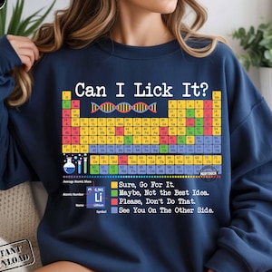 May include: Navy blue sweatshirt with the text "Can I Lick It?" above a periodic table of elements. The sweatshirt also has the text "Sure, Go For It. Maybe, Not the Best Idea. Please, Don't Do That. See You On The Other Side."
