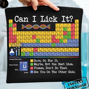 Op de afbeelding: Zwart grafisch T-shirt met de tekst "Can I Lick It?" en een periodiek systeem ontwerp. Bevat de tekst "Sure, Go For It." en "See You On The Other Side."