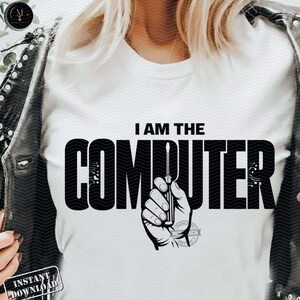May include: A white t-shirt featuring the black text I AM THE COMPUTER in a bold, stylized font. The letter U is replaced by a graphic illustration of a hand holding a screwdriver. The design is centered on the chest of the garment.