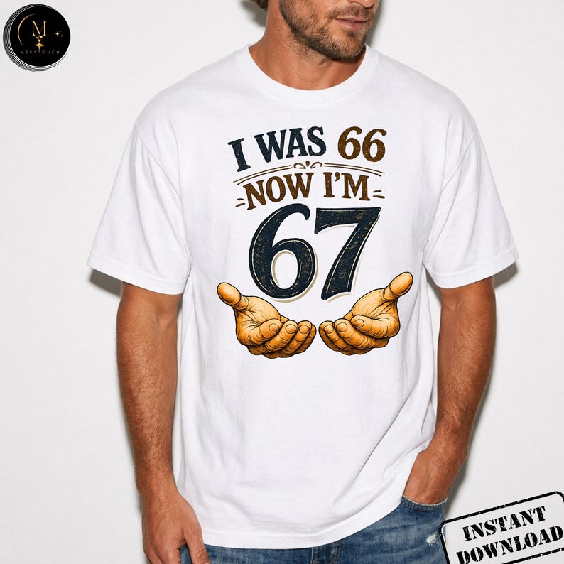 Puede incluir: Camiseta blanca con el texto "I WAS 66 NOW I'M 67" en negro y marr&oacute;n. El n&uacute;mero 67 est&aacute; en una fuente grande y en negrita. Debajo del texto hay dos manos abiertas en un tono c&aacute;lido anaranjado.