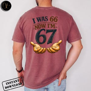 Puede incluir: Camiseta granate con el texto "I WAS 66 NOW I'M 67" en marr&oacute;n y negro. El n&uacute;mero 67 es grande y negro, con dos manos abiertas debajo. La camiseta es un dise&ntilde;o tem&aacute;tico de cumplea&ntilde;os.