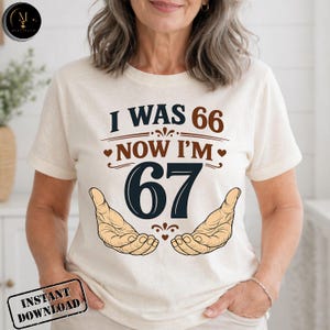 Puede incluir: Camiseta color crema con el texto "I WAS 66 NOW I'M 67" en marr&oacute;n y azul marino. El dise&ntilde;o incluye dos manos y elementos decorativos. La camiseta tambi&eacute;n tiene un sello "INSTANT DOWNLOAD".