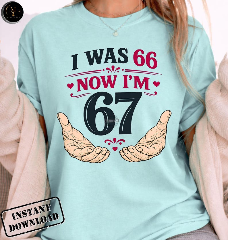 Puede incluir: Camiseta azul claro con el texto "I WAS 66 NOW I'M 67" en negro y rojo. El n&uacute;mero 67 es grande y centrado, con dos manos a cada lado. La camiseta tiene un gr&aacute;fico de "Descarga instant&aacute;nea".