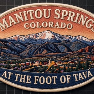May include: An oval embroidered patch featuring a landscape of Manitou Springs, Colorado, with snow-capped mountains, a town scene, and the text "MANITOU SPRINGS COLORADO" at the top and "AT THE FOOT OF TAVA" at the bottom in cream-colored thread.