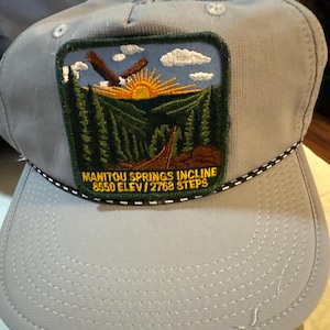 May include: A white ceramic mug with a black handle and the text "But First, Coffee" in a bold, black font. The mug is set against a blurred background, suggesting a cozy setting.